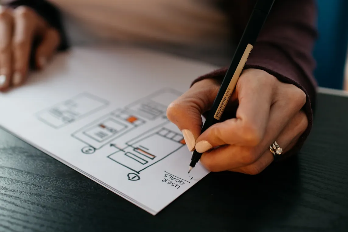 Wireframes sketched on paper beside a laptop